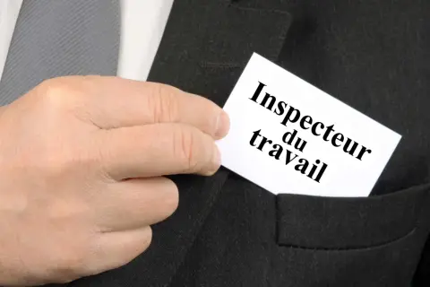 Main d'un homme glissant une carte "Inspecteur du travail" dans la poche d'un costume.