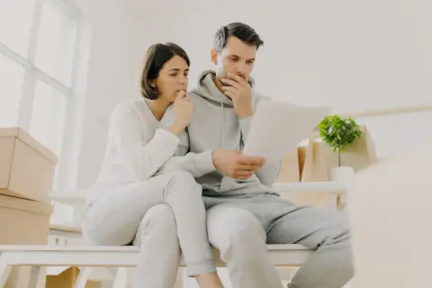 Couple inquiet, entouré de cartons, face à un loyer impayé locataire en détresse. Ils semblent préoccupés par des documents.
