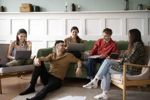 Cinq jeunes discutent et travaillent ensemble dans un salon, une scène typique d'une colocation avec un bail solidaire.
