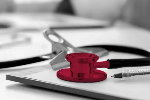 Un stéthoscope rouge vif sur un presse-papiers, prêt pour une visite médicale. Un stylo et une pince complètent la scène.