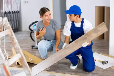 Un ouvrier montre une lame de parquet à une cliente. Ces travaux réalisés par le propriétaire sont déductibles.