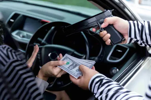 Un homme en pull rayé menace une personne en voiture avec un pistolet, exigeant de l'argent. Scène d'extorsion.
