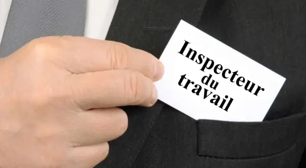 Main d'un homme glissant une carte "Inspecteur du travail" dans la poche d'un costume.
