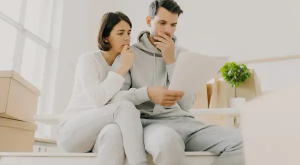 Couple inquiet, entouré de cartons, face à un loyer impayé locataire en détresse. Ils semblent préoccupés par des documents.