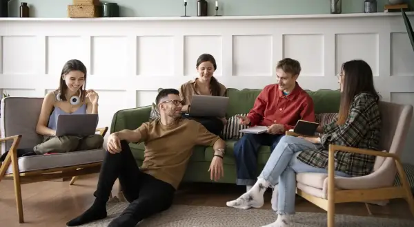 Cinq jeunes discutent et travaillent ensemble dans un salon, une scène typique d'une colocation avec un bail solidaire.