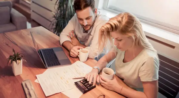 Couple calculant la refacturation de la taxe foncière pour un bail commercial, avec un ordinateur portable et des documents sur la table.