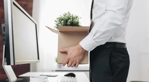 Un employé quitte son bureau, emportant ses affaires dans un carton. Il s'apprête à recevoir son solde tout compte imposable.