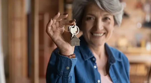 Une femme souriante de plus de 65 ans tient des clés avec un pendentif maison. Elle bénéficie de la **loi alur locataire plus de 65 ans**.