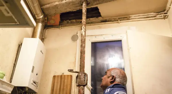 Un homme regarde un plafond délabré soutenu par une poutre rouillée. Ce **logement insalubre** montre des signes de dégradation avancée.