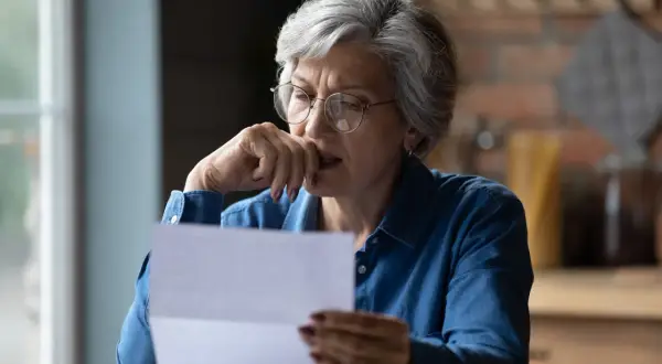 Femme âgée inquiète lisant une lettre, peut-être une facture de taxe foncière.