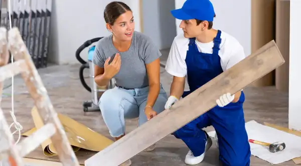 Un ouvrier montre une lame de parquet à une cliente. Ces travaux réalisés par le propriétaire sont déductibles.